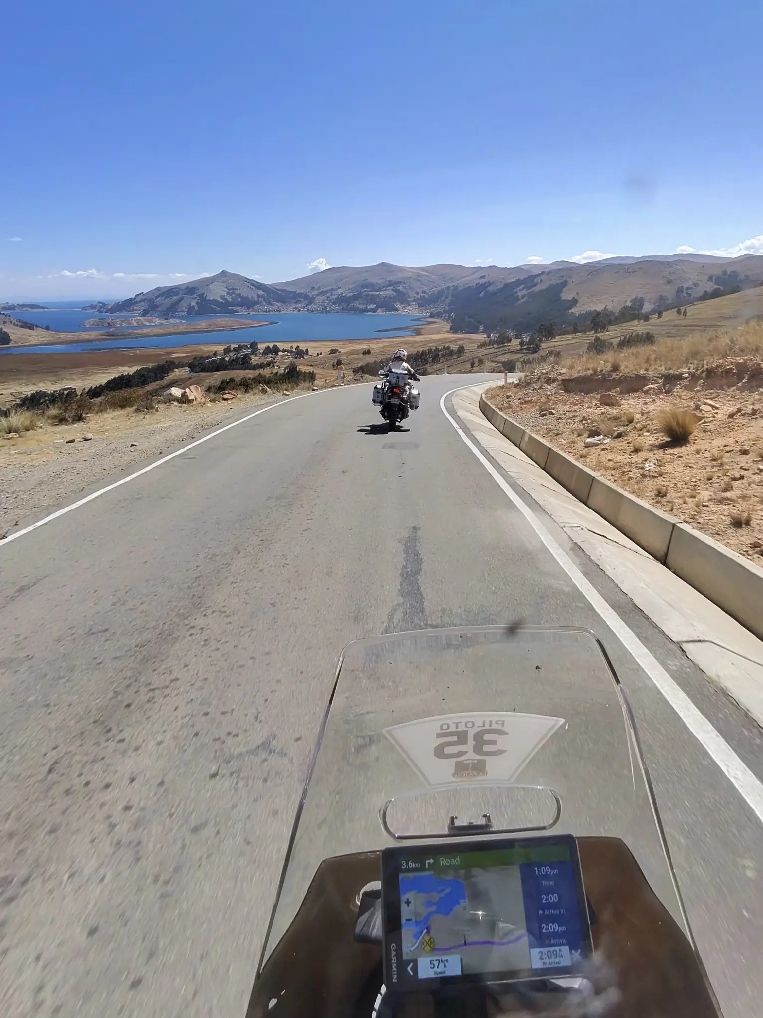 View from a motorcycle on a scenic road heading toward a mountain lake during an exciting motorcycle trip across South America.