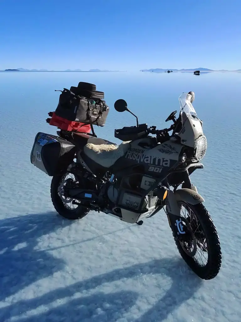 Husqvarna 701 motorcycle trip bike reflecting perfectly on the shallow water of Uyuni Salt Flats under a deep blue sky.